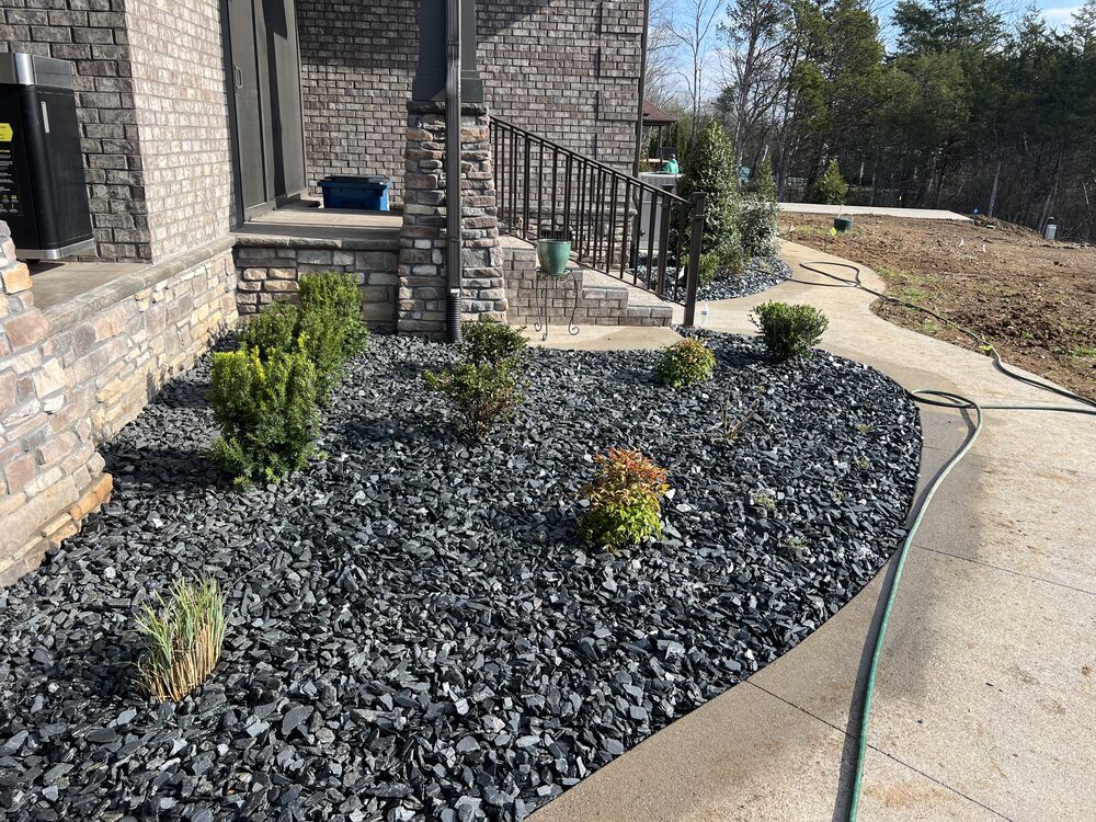 Black rock landscape bed along home foundation with steps