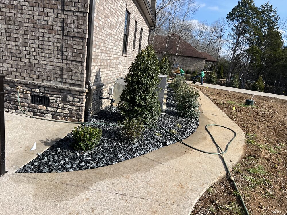 Black rock landscape bed along walkway with mixed shrubs